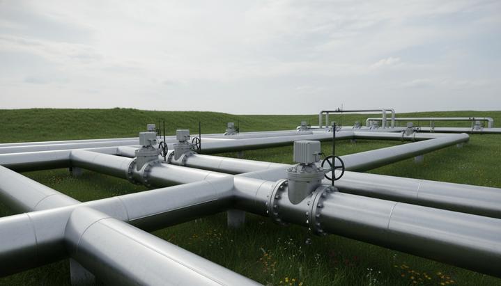 Сеть новых стальных трубопроводов большого диаметра с клапанами и датчиками, проходящая через зеленые холмы под пасмурным небом.